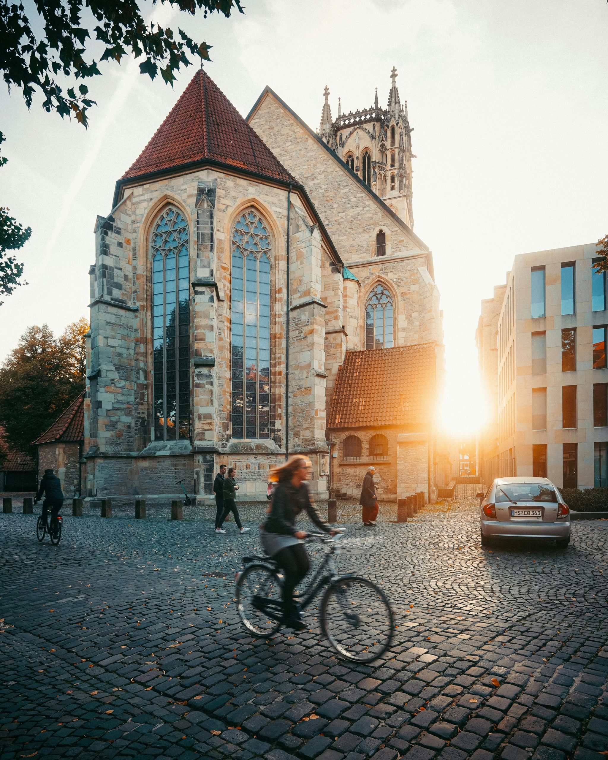 A vibrant street scene with a cyclist and pedestrians near a gothic cathedral at sunset.