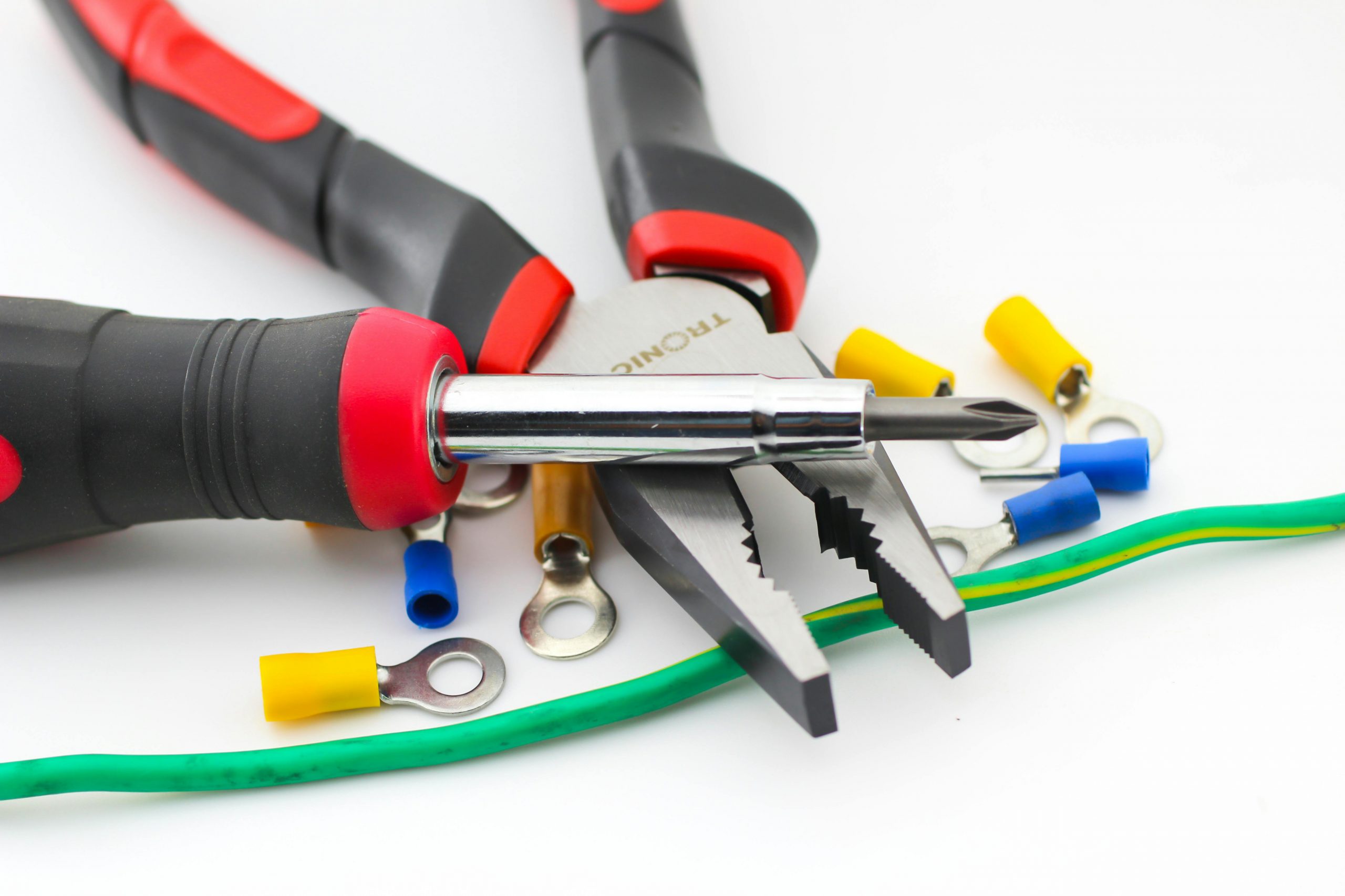 Close-up image of pliers and screwdriver with colorful wire connectors on a white background.